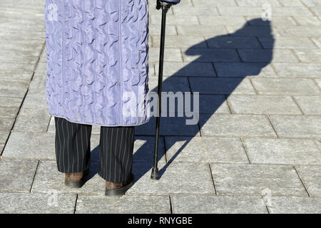 Alte Frau mit einem Stock, lange Schatten auf Pflaster. Konzept für Alter, Erkrankungen der Wirbelsäule, ältere oder blinde Person Stockfoto