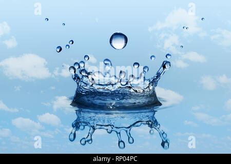 Fallende Tropfen Regen mit Wasser spritzen in Krone gestalten. Blauer Himmel und weiße Wolken als Hintergrund. Stockfoto