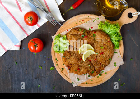 Große Wiener Schnitzel auf einem Holzbrett mit Zitrone auf einem dunklen Hintergrund. Fleischgericht. Ansicht von oben, flach. Stockfoto