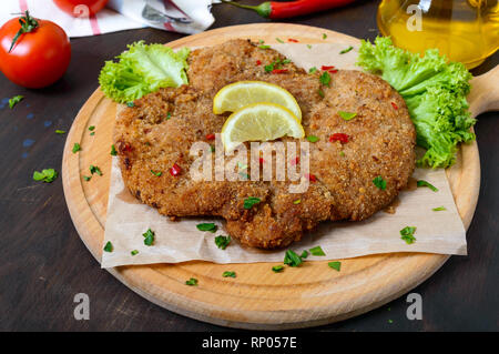 Große Wiener Schnitzel auf einem Holzbrett mit Zitrone auf einem dunklen Hintergrund. Fleischgericht Stockfoto