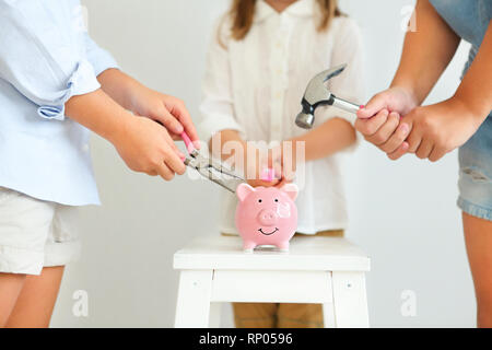 Kinder mit Schraubendreher, Zange und Hammer durch den Pink Pig piggy Bank auf weißem Hintergrund Stockfoto