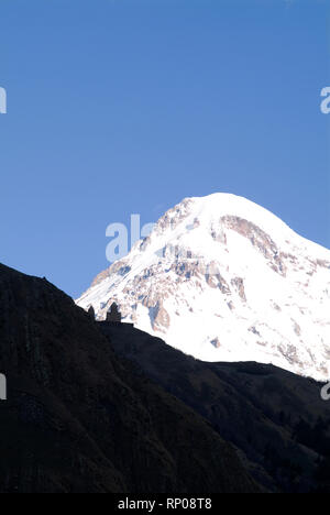 Mt. Kazbek (5033 m Höhe) ist der dritthöchste Berg in Georgia, mit der Silhouette des 14. Jahrhunderts Tsminda Sameba (Heilige Dreifaltigkeit) Kirche Stockfoto