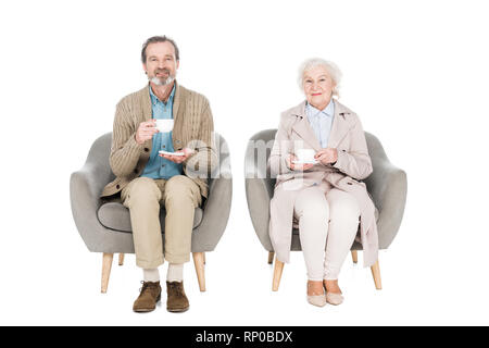 Gerne älteres Paar hält Tassen mit Tee während der Sitzung in Sesseln isoliert auf weißem Stockfoto