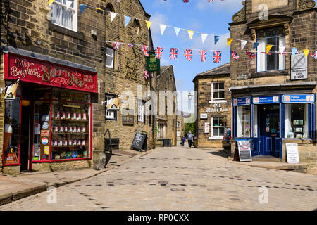 Traditionelle Sweet Shop, historische Gasthäuser, touristische Informationen & Bunting über gepflasterten Straße - Hauptstraße, Haworth Village, West Yorkshire, England, UK. Stockfoto