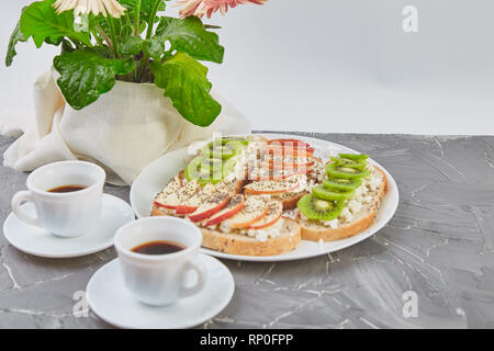 Gesundes Frühstück Kaffee, Blumenstrauß aus Blume und Toast mit Kiwi, Apfel, Hüttenkäse und Chia Samen auf grauem Hintergrund. Kopieren Sie Platz. Stockfoto