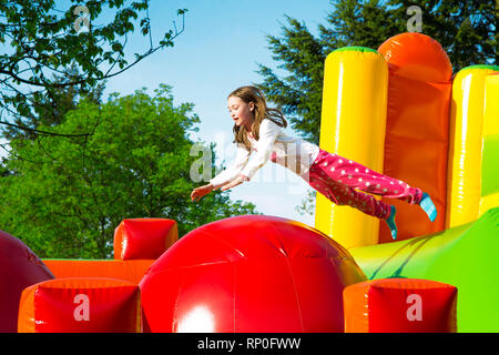 Gerne kleine Mädchen haben viel Spaß beim von Ball zu Ball springen auf ein Schloss aufpumpen. Stockfoto