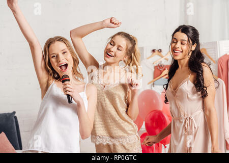 Schönen Lächeln multiethnischen Mädchen in Nachtwäsche Karaoke singen an pyjamaparty im Schlafzimmer Stockfoto