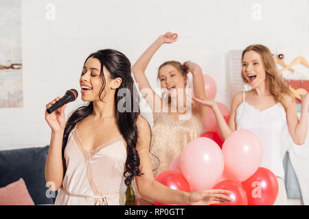 Schöne multiethnischen Mädchen in Nachtwäsche Karaoke singen an pyjamaparty im Schlafzimmer Stockfoto