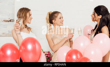 Schöne multikulturelle Mädchen in Nachtwäsche feiern mit Sekt und Ballone während Pyjamaparty Stockfoto