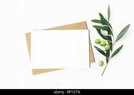 Feminine Schreibwaren, desktop Mock-up-Szene. Leere horizontale Grußkarte und Handwerk Umschlag mit Olive Branch. weißem Hintergrund. Flach, oben Stockfoto