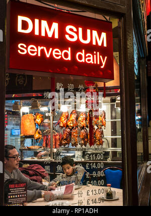 DIM SUM TÄGLICHE DÄMMERUNG NACHT chinesische Restaurant Fenster 'Lotus Garden" mit Diners. Beleuchtete Zeichen mit 'Dim Sum serviert täglich "Gerrard Street Chinatown Soho London UK Stockfoto