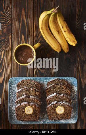 In Scheiben geschnittene hausgemachte Kuchen an braun blau Teller dekoriert mit drei Bananen und Tasse schwarzen Kaffee. Vertikale. Kopieren Sie Platz Stockfoto