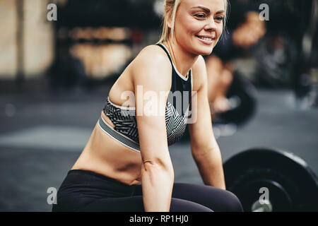 Passen junge Frau in Sportkleidung lächelnd während der Vorbereitung zum Training mit schweren Gewichten an der Turnhalle Stockfoto