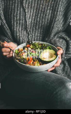 Gesunde vegetarische Abendessen. Frau in Grau jeans und warmen Pullover holding Schüssel mit frischem Salat, Avocado, Körner, Bohnen, gebratenes Gemüse. Superfood, Stockfoto
