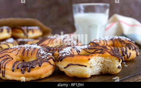 Hausgemachte klassische Donuts mit Schokolade und Kokos Flocken und ein Glas Milch auf einem dunklen Hintergrund. Close Up. Stockfoto