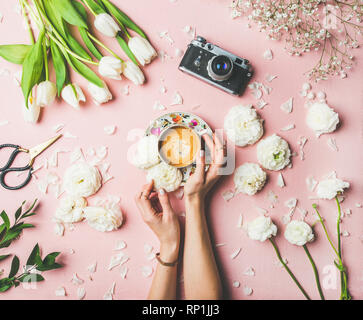 Frühling bunte Layout. Flachbild-lay weiblicher Hände, die Tasse Kaffee, Schere, Filmkamera, Weiße Tulpen und buttercup Blumen auf rosa Hintergrund Stockfoto