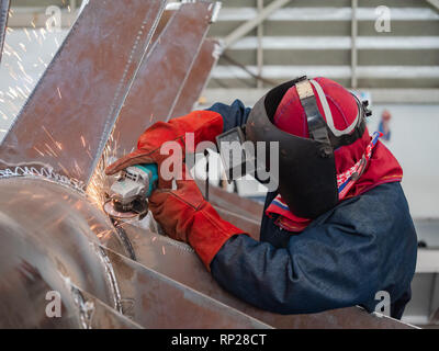 Industrielle Arbeiter tragen eine Maske mit einem Winkelschleifer auf einer Stahlkonstruktion. Stockfoto