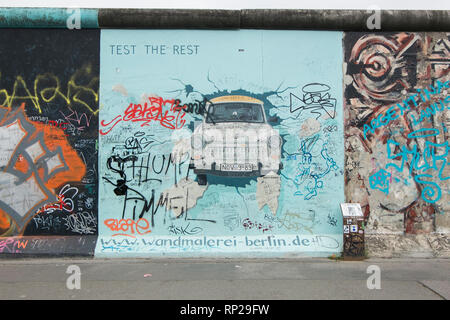 Die knarrenden Ostdeutschen auto Trabant macht ein Auftritt auf der Berliner Mauer in Berlin, Deutschland. Stockfoto