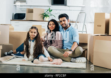 Latin, Mann und Frau in Teppich in der Nähe der Tochter sitzen im neuen Haus Stockfoto