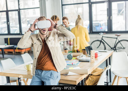 Überrascht männlichen Designer gestikulierte mit Händen, während in der virtuellen Realität im Loft Büro mit den Kollegen Hintergrund Stockfoto