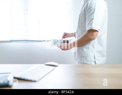 Arzt im Computer tablet einheitliche Neben seinem Büro Schreibtisch im Krankenhaus Stockfoto