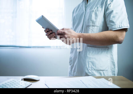 Arzt im Computer tablet einheitliche Neben seinem Büro Schreibtisch im Krankenhaus Stockfoto