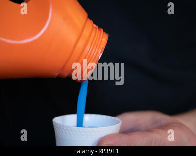In der Nähe von kleinen Teil Cap von flüssigem Waschmittel und Blau gel Flüssigkeit Gießen von Kunststoff Flasche. isolierte Bild auf schwarzem Hintergrund Stockfoto