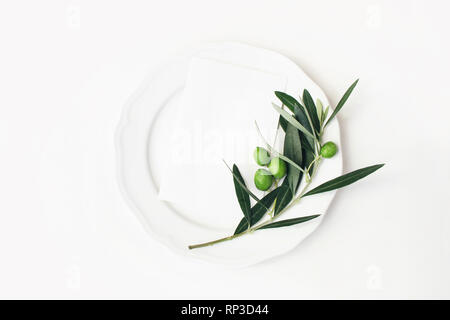 Festliche Tafel Sommer Einstellung mit Olivenöl, Blätter, Zweig und Obst auf Porzellan Teller. Leeres Papier Karte mockup Szene. Mittelmeer Hochzeit oder Stockfoto