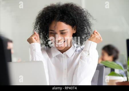 Afrikanisches Mixed Race weiblichen am Schreibtisch im Büro suchen auf Laptop Bildschirm fühlt sich glücklich. Kopf geschossen Portrait schwarz tausendjährigen Mitarbeiter erhielt lange ein Stockfoto