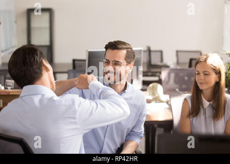 Mann Arbeiter sitzen auf Stuhl Faust stoßen mit Kollege Begrüßung zu Beginn des Arbeitstages. Glückliche Mitarbeiter erreicht Shared Business g Stockfoto