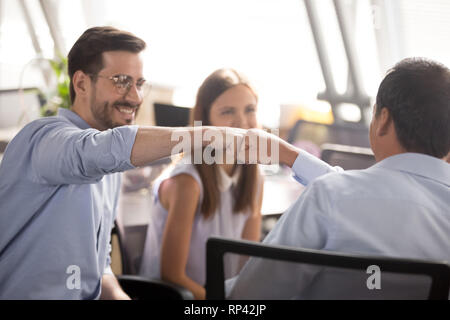 Tausendjährige fröhliche positive männliche Kollegen sitzen auf Stühlen im Coworking Bereich Faust zusammen, konzentrieren Sie sich auf die Hände schließen. Konzept der Begrüßung oder Stockfoto