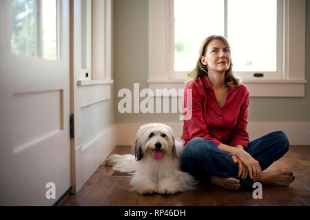 Frau mittleren Alters sieht nachdenklich, als sie sitzt auf dem Boden neben Ihrem Hund. Stockfoto