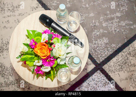 Herrlich bunten Strauß mit bunten Rosen. Blumenschmuck auf hölzernen Tisch mit Gläsern und drahtloses Mikrofon - Wissenschaftliche Konferenz Stockfoto