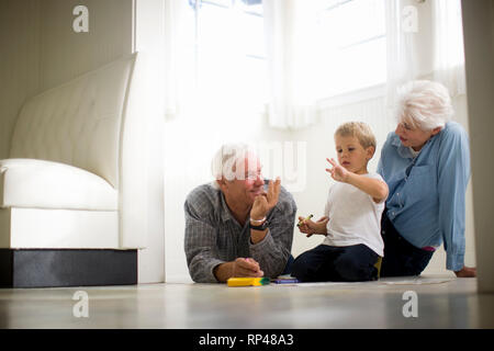 Junge Junge sitzt auf dem Boden mit seinen Großeltern. Stockfoto