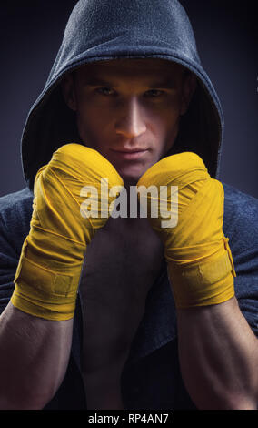 Muskulöse Boxer in einer Haube mit starken Hände und geballten Fäusten auf schwarzem Hintergrund Stockfoto