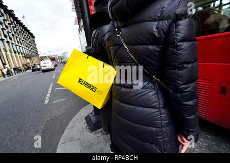 London, England, UK. Frau mit einem Selfridges Tragetasche Überqueren der Straße in Parliament Square Stockfoto