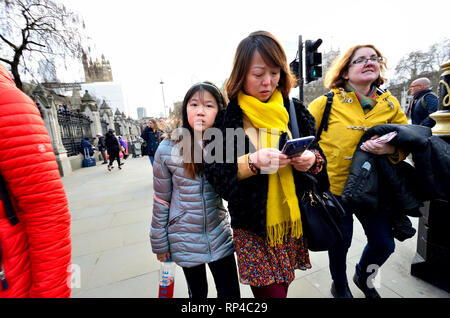 London, England, UK. Asiatische Mutter und Tochter zu Fuß auf der Straße - die Mutter an ihr Mobiltelefon suchen, Parliament Square Stockfoto