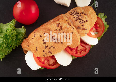 Croissant Sandwich mit Salat Mozzarella und Tomaten über schwarzen Stein. Gesunden Snack. Ansicht von oben. Stockfoto