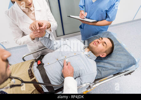 7/8-Ansicht von Ärzten und kranken Patienten, der auf einer Trage in der Klinik Stockfoto