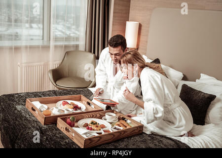 Paar essen Frühstück im Bett und beobachtete Film auf Tablet Stockfoto