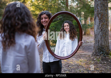 Fröhliche junge Frau, Reflexion der Zwillingsschwester im Herbst Tag im Wald Stockfoto