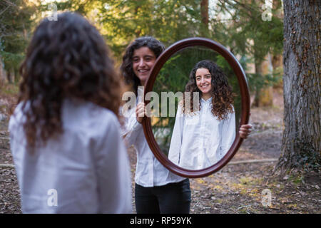 Fröhliche junge Frau, Reflexion der Zwillingsschwester im Herbst Tag im Wald Stockfoto