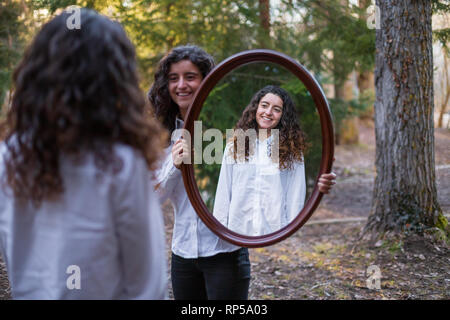 Fröhliche junge Frau, Reflexion der Zwillingsschwester im Herbst Tag im Wald Stockfoto