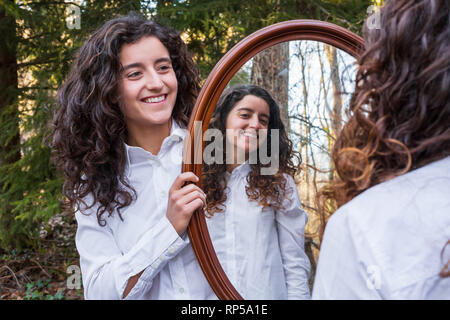 Fröhliche junge Frau, Reflexion der Zwillingsschwester im Herbst Tag im Wald Stockfoto