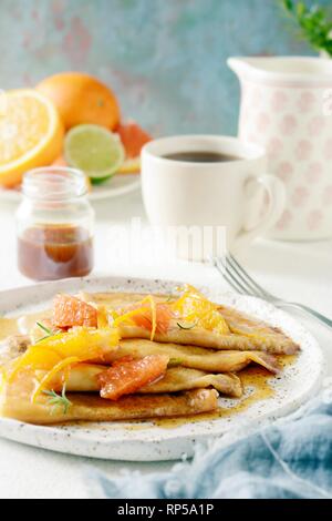 Pfannkuchen Crepe Suzette zum Frühstück mit orange Karamell-sauce, Orangenscheiben, Kalk und Orangenschale und eine Tasse Kaffee. Dessert französische Küche. Sunda Stockfoto