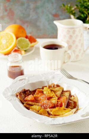 Pfannkuchen Crepe Suzette zum Frühstück mit orange Karamell-sauce, Orangenscheiben, Kalk und Orangenschale und eine Tasse Kaffee. Dessert französische Küche. Sunda Stockfoto