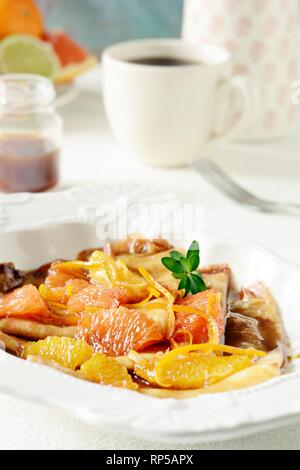 Pfannkuchen Crepe Suzette zum Frühstück mit orange Karamell-sauce, Orangenscheiben, Kalk und Orangenschale und eine Tasse Kaffee. Dessert französische Küche. Sunda Stockfoto