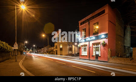 Englischer Pub in der Nacht auf kleinen Straße mit langen Belichtungszeiten Verkehr vorbei Stockfoto