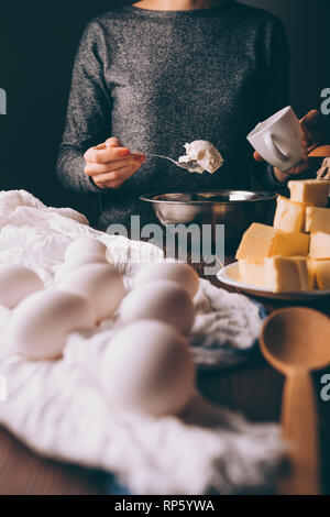 Junge Frau Kochen Teig für Kreis Gießen Sauerrahm in Metall Schüssel Neben Eiern und gewürfelte Butter auf braune Holztisch. Stockfoto