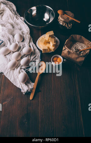 Blick von oben auf die Utensilien und Zutaten zum Kochen Kuchen auf dunkelbraunen hölzernen Tisch. Rustikale hausgemachte Backwaren. Stockfoto